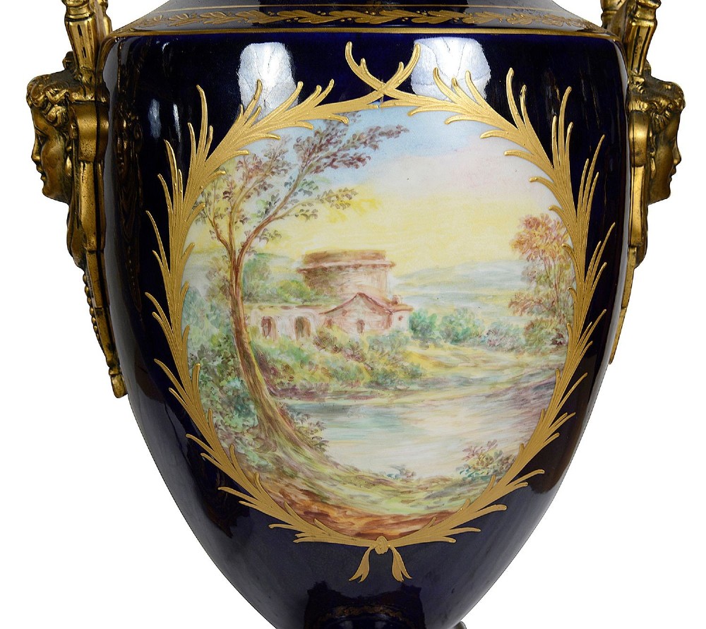 A pair of 19th-century French Sevres-style cobalt blue porcelain urn lamps featuring hand-painted romantic scenes, ornate gilt bronze mounts, and fringed fabric shades. View XI