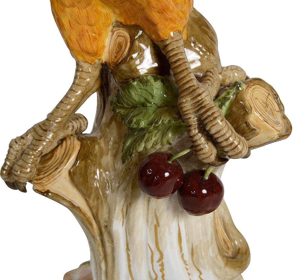 A polychrome porcelain figurine of a parrot with blue, green, and yellow feathers perched on a tree stump. View VII