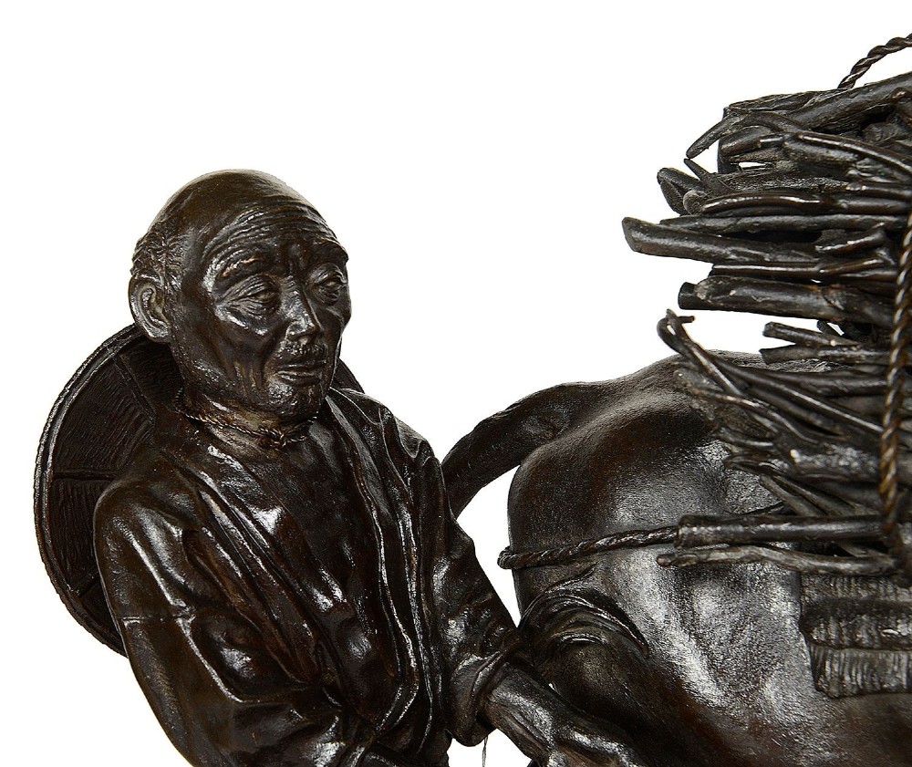 A dark patinated bronze Meiji period sculpture depicting a woodsman guiding a water buffalo laden with firewood, mounted on a rustic carved burr wood base. View V