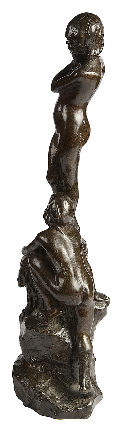 A dark brown patinated bronze sculpture depicting two young children near a rock formation, with one standing above holding a towel and the other crouching at the base. View VI