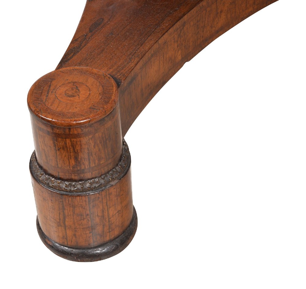 A circular Regency period timber centre table featuring a floral brass inlaid border, a central tapered pedestal stem, and a tripartite base resting on cylindrical feet with castors. View VI