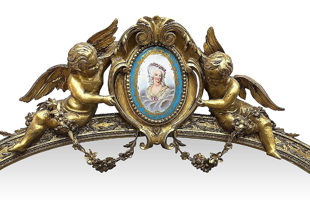 A large gilt-bronze wall mirror featuring an arched crest with sculpted putti, foliage mouldings, and oval Sevres porcelain plaques set along the frame. View II