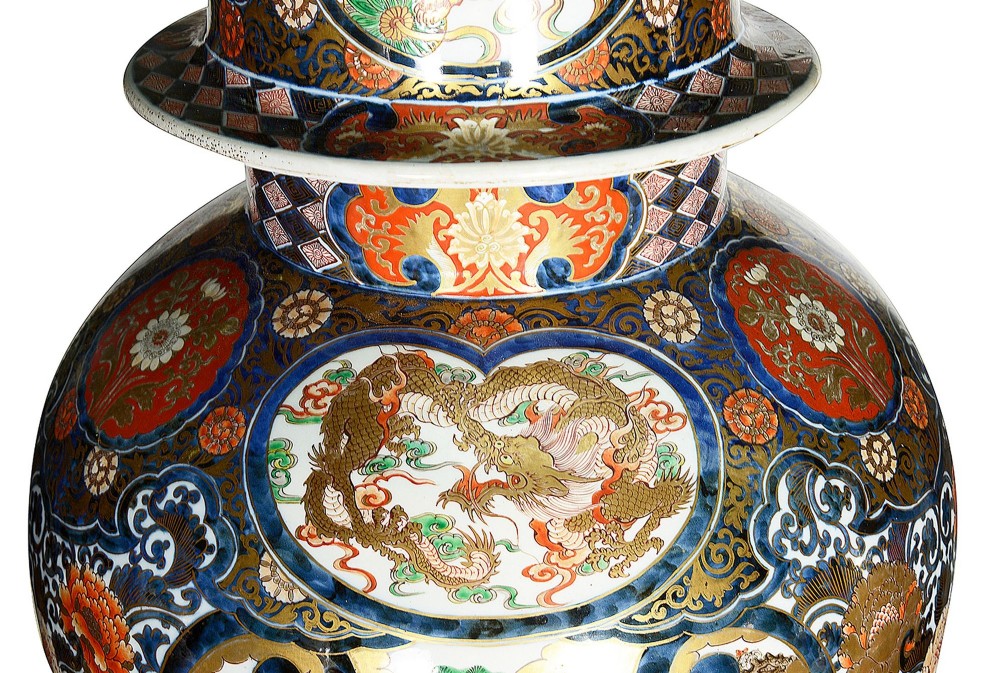 A pair of large 19th-century Japanese Imari porcelain lidded vases featuring painted reserves depicting figures in garden settings, surrounded by cobalt blue, orange, green, and gold patterns. View V