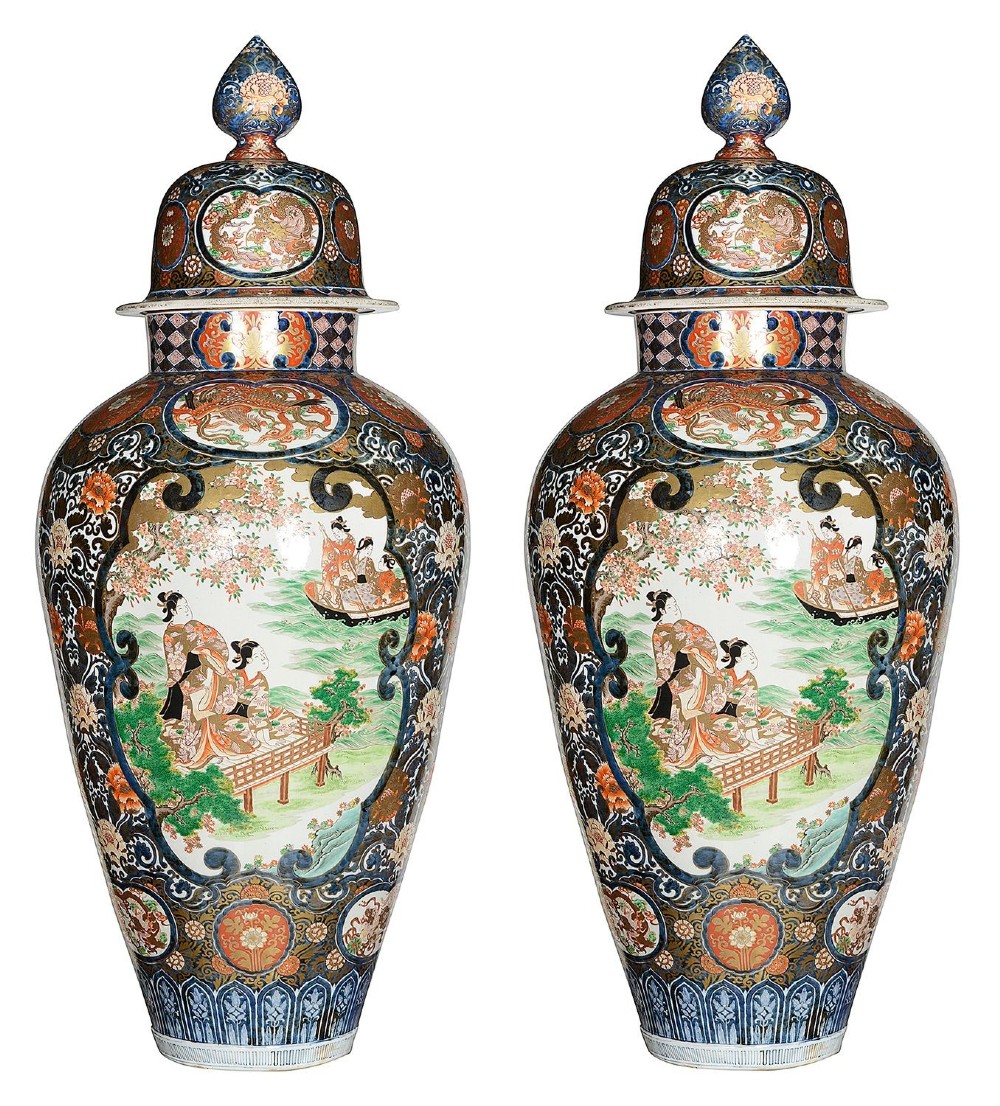 A pair of large 19th-century Japanese Imari porcelain lidded vases featuring painted reserves depicting figures in garden settings, surrounded by cobalt blue, orange, green, and gold patterns. View VII