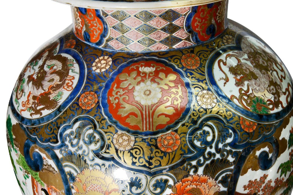 A pair of large 19th-century Japanese Imari porcelain lidded vases featuring painted reserves depicting figures in garden settings, surrounded by cobalt blue, orange, green, and gold patterns. View XI