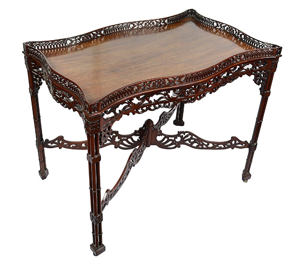 A dark mahogany Chippendale style silver table featuring a serpentine top, pierced fretwork gallery, pierced apron, and cluster legs with an X-stretcher.