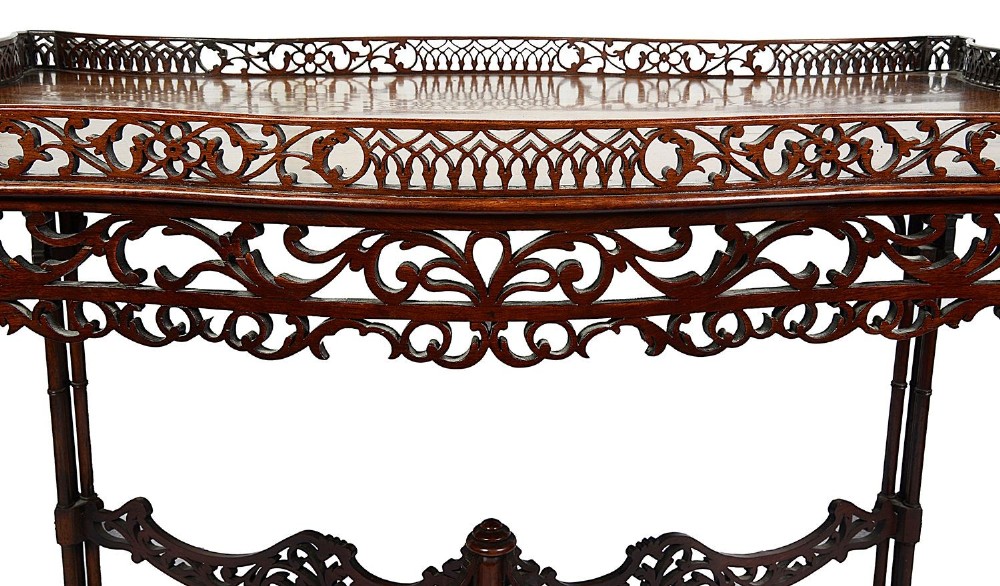 A dark mahogany Chippendale style silver table featuring a serpentine top, pierced fretwork gallery, pierced apron, and cluster legs with an X-stretcher. View IV
