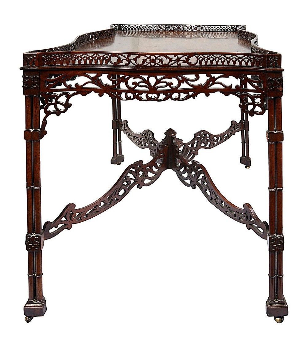 A dark mahogany Chippendale style silver table featuring a serpentine top, pierced fretwork gallery, pierced apron, and cluster legs with an X-stretcher. View V
