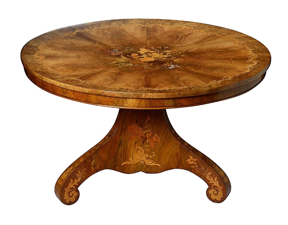 A circular Victorian walnut centre table featuring radial segment veneers, intricate floral marquetry, and a carved pedestal base with scroll feet.