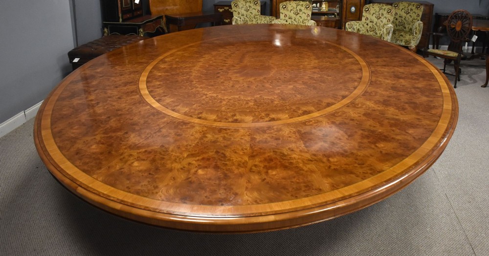 A large oval burr walnut extending dining table featuring decorative satinwood crossbanding and pedestal legs fitted with brass castors. View VII