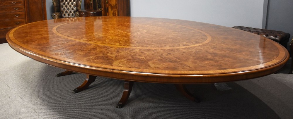 A large oval burr walnut extending dining table featuring decorative satinwood crossbanding and pedestal legs fitted with brass castors. View VIII