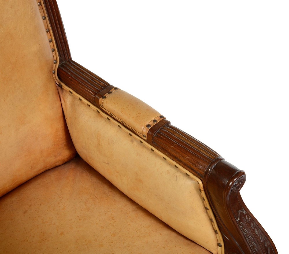 A pair of Regency style dark mahogany library armchairs upholstered in tan leather with brass stud trimming and reeded carved legs. View V