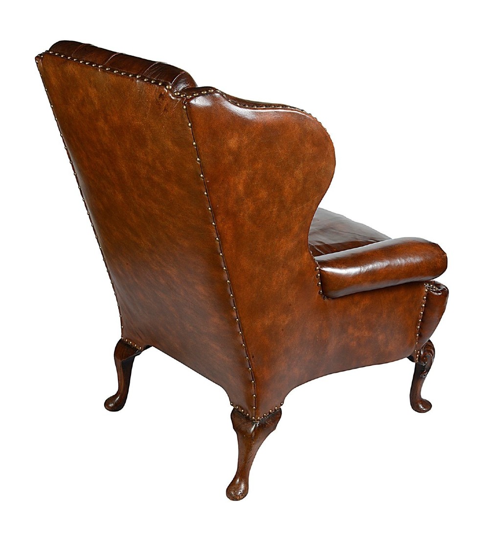 A pair of Georgian style chestnut brown leather wingback armchairs featuring deep button tufting, brass stud trimming, and carved cabriole legs. View IV