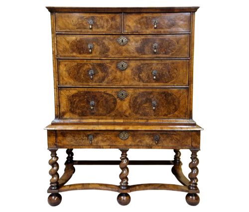 fig 1. An antique William and Mary burr walnut chest on stand featuring multiple drawers, brass teardrop handles, barley twist legs, curved stretchers, and ball feet.