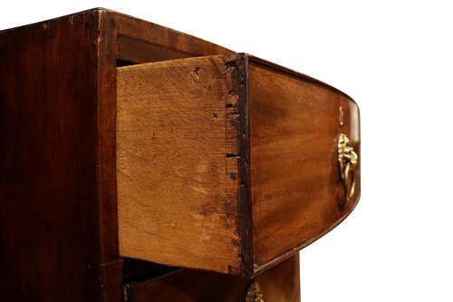 fig 2. A George III bow-fronted mahogany chest of drawers featuring two short over two long drawers with brass lion mask ring handles and splayed feet.