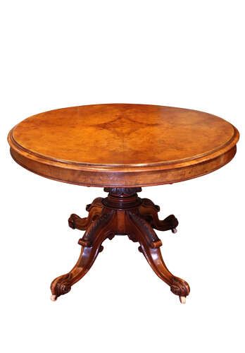 fig 1. A Victorian burr walnut oval tilt-top loo table featuring quarter-matched grain patterns, displayed vertically on a carved base with castors.