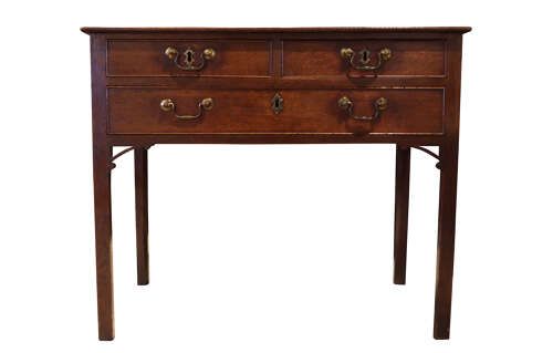 fig 1. A George III dark oak lowboy featuring a rectangular top over three drawers with brass swan-neck handles, supported on straight square legs.