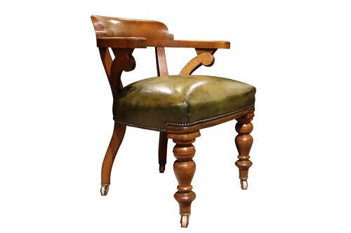 fig 1. A Victorian golden oak library chair featuring a curved backrest, turned front legs with castors, and an olive green leather seat trimmed with brass studs.