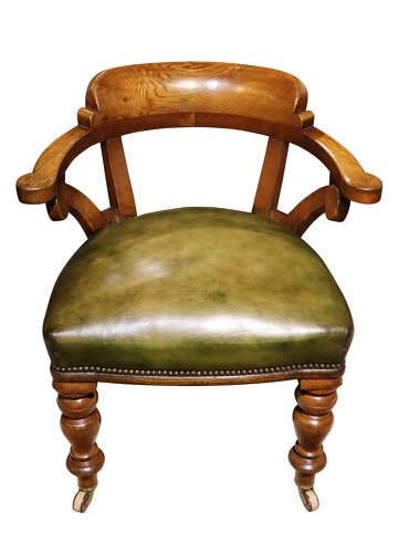 fig 2. A Victorian golden oak library chair featuring a curved backrest, turned front legs with castors, and an olive green leather seat trimmed with brass studs.