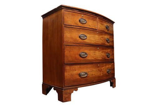 fig 1. A Regency period bow-front mahogany chest of drawers featuring two short drawers over three long drawers with oval brass handles and bracket feet.