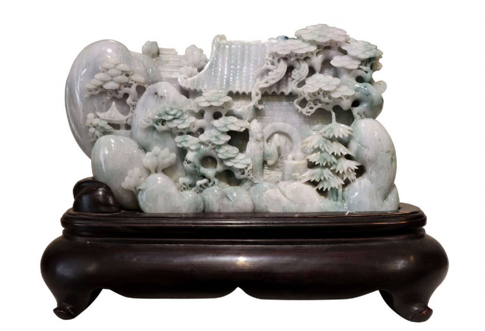 An intricate Chinese pale green carved jade mountain sculpture depicting pavilions and pine trees resting on a fitted dark hardwood base.
