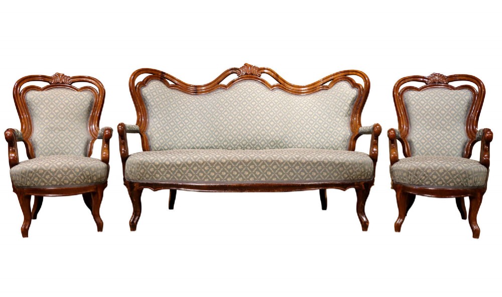 A late 19th-century three-piece walnut salon suite featuring a central settee and two matching armchairs upholstered in patterned sage green fabric with carved serpentine frames.