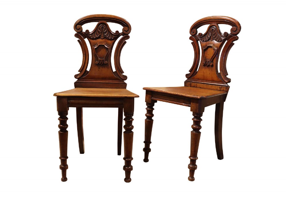 A pair of mid-Victorian mahogany hall chairs with carved shield backrests, solid seats, and turned front legs.