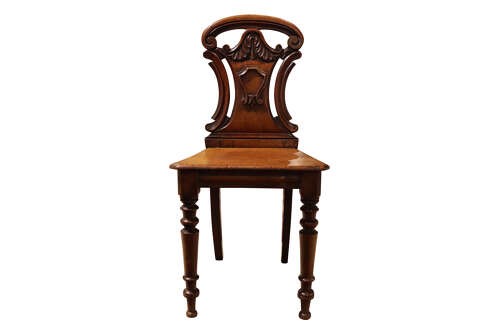 A pair of mid-Victorian mahogany hall chairs with carved shield backrests, solid seats, and turned front legs. View V