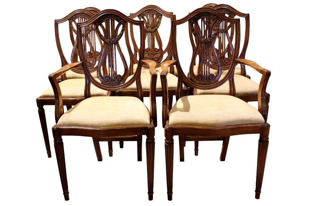 Set of mahogany dining chairs featuring shield-shaped backs with carved lyre motifs, fluted front legs, and neutral upholstered seats.