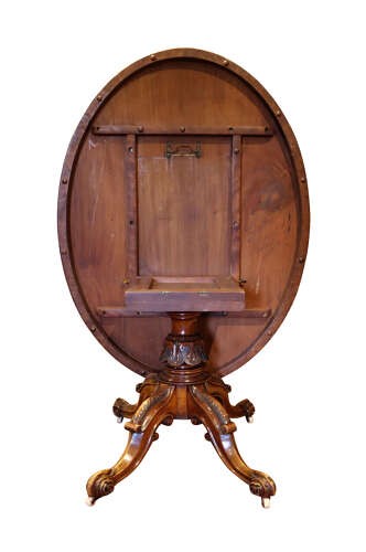 A Victorian burr walnut oval tilt-top loo table featuring quarter-matched grain patterns, displayed vertically on a carved base with castors. View V