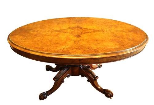 A Victorian burr walnut oval tilt-top loo table featuring quarter-matched grain patterns, displayed vertically on a carved base with castors. View VI