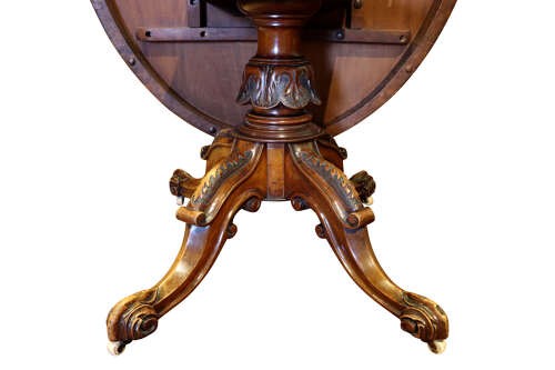 A Victorian burr walnut oval tilt-top loo table featuring quarter-matched grain patterns, displayed vertically on a carved base with castors. View VII