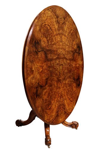 A Victorian oval burr walnut breakfast table featuring rich timber grain and a carved quadrapod base with scroll feet. View V