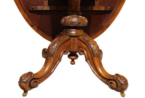 A Victorian oval burr walnut breakfast table featuring rich timber grain and a carved quadrapod base with scroll feet. View VII