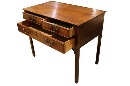 A George III dark oak lowboy featuring a rectangular top over three drawers with brass swan-neck handles, supported on straight square legs. View V
