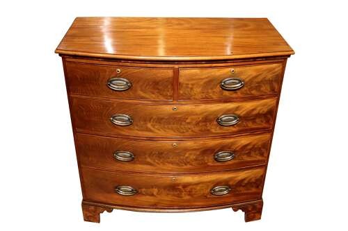 A Regency period bow-front mahogany chest of drawers featuring two short drawers over three long drawers with oval brass handles and bracket feet. View III