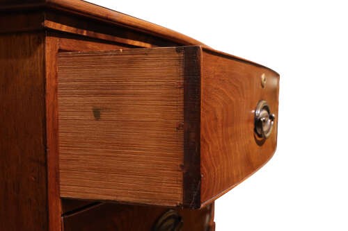 A Regency period bow-front mahogany chest of drawers featuring two short drawers over three long drawers with oval brass handles and bracket feet. View V
