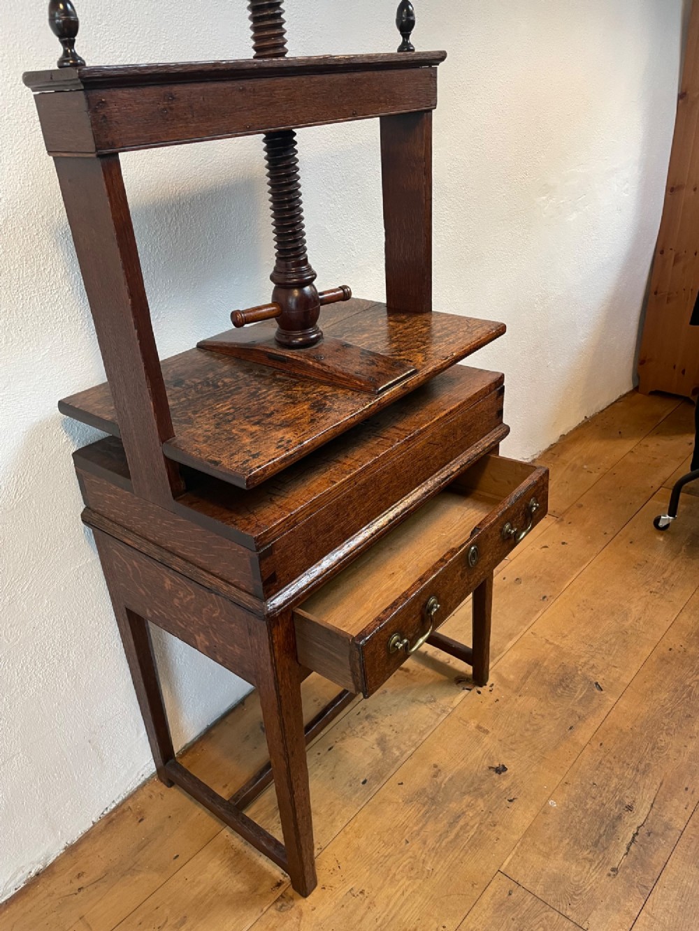 A dark oak Georgian linen press featuring a central wooden screw mechanism over a single drawer table stand with turned finials and brass handles. View II