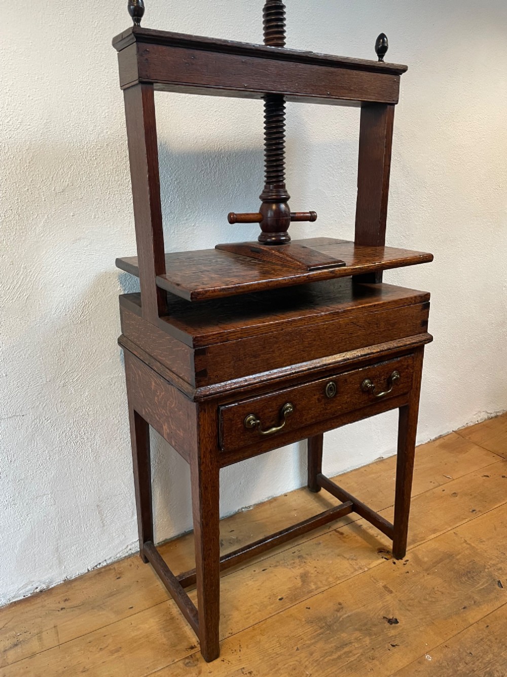 A dark oak Georgian linen press featuring a central wooden screw mechanism over a single drawer table stand with turned finials and brass handles. View III