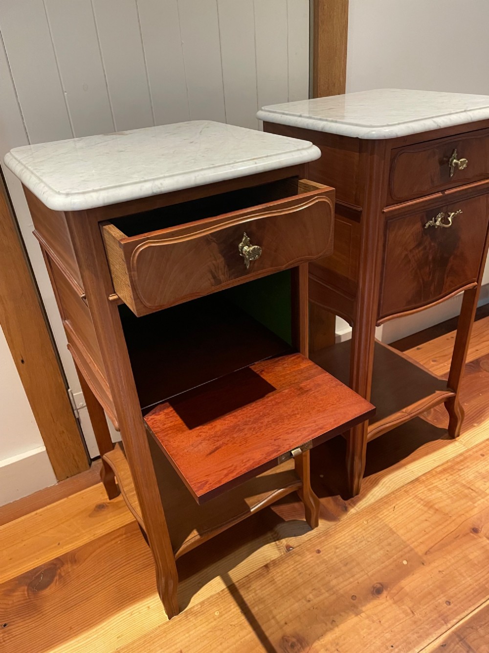 A pair of tall French wooden bedside cupboards featuring inset white marble tops, single drawers, cupboard doors, and lower open shelves. View II