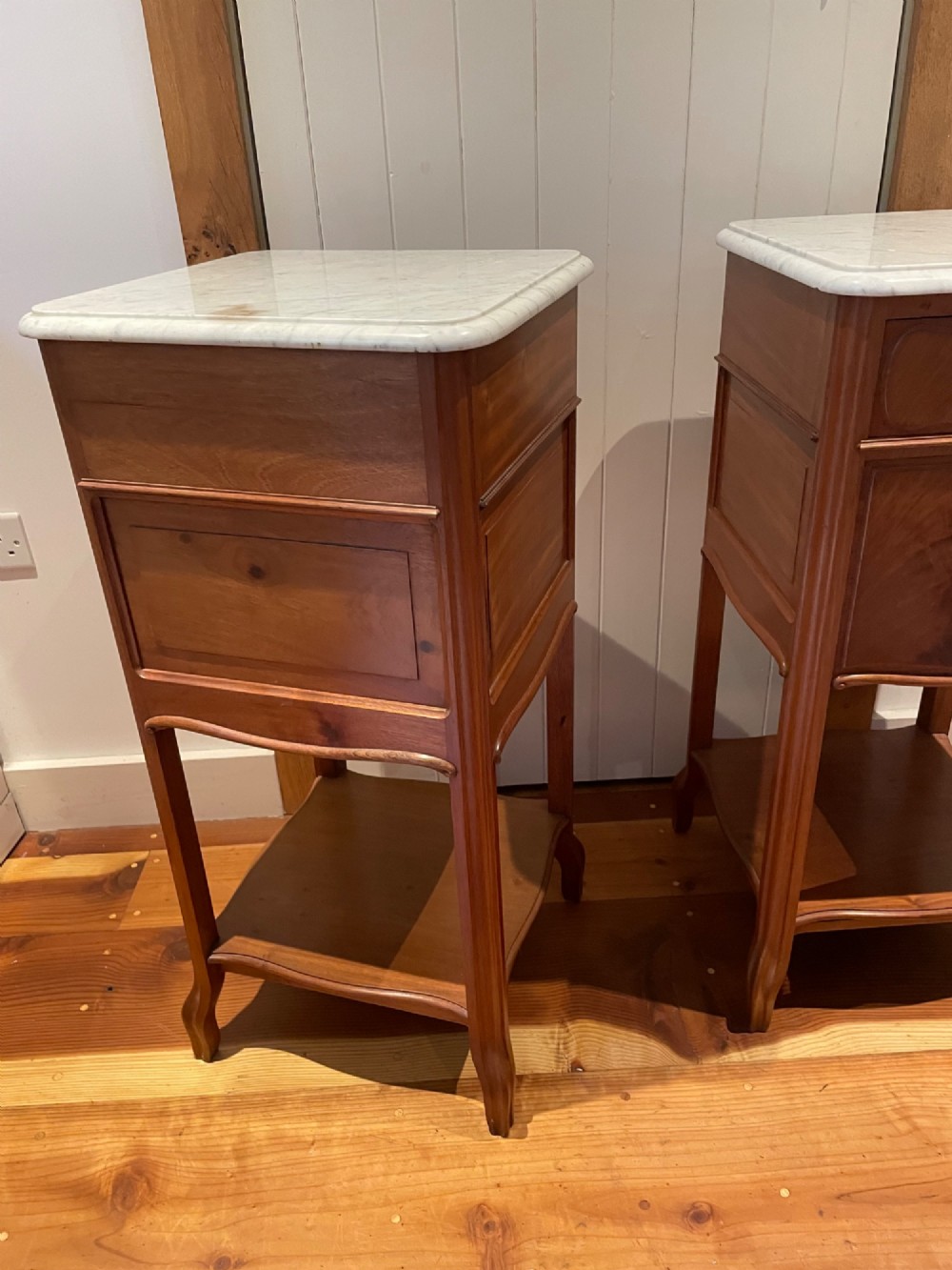 A pair of tall French wooden bedside cupboards featuring inset white marble tops, single drawers, cupboard doors, and lower open shelves. View III