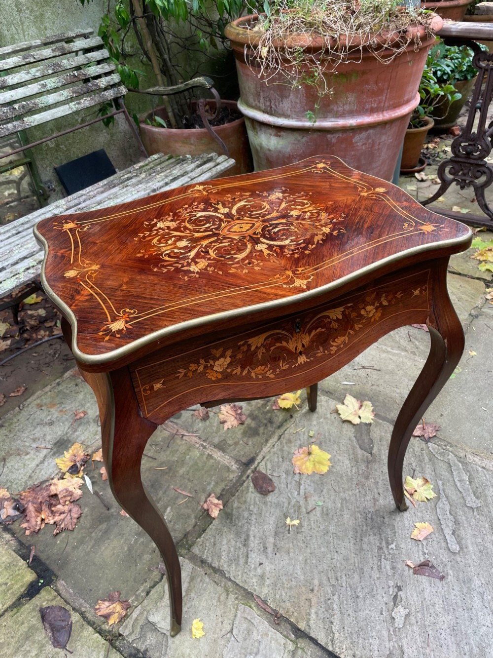 A late 19th-century French marquetry sewing table featuring floral wood inlay on a serpentine top, brass edging, and slender cabriole legs.