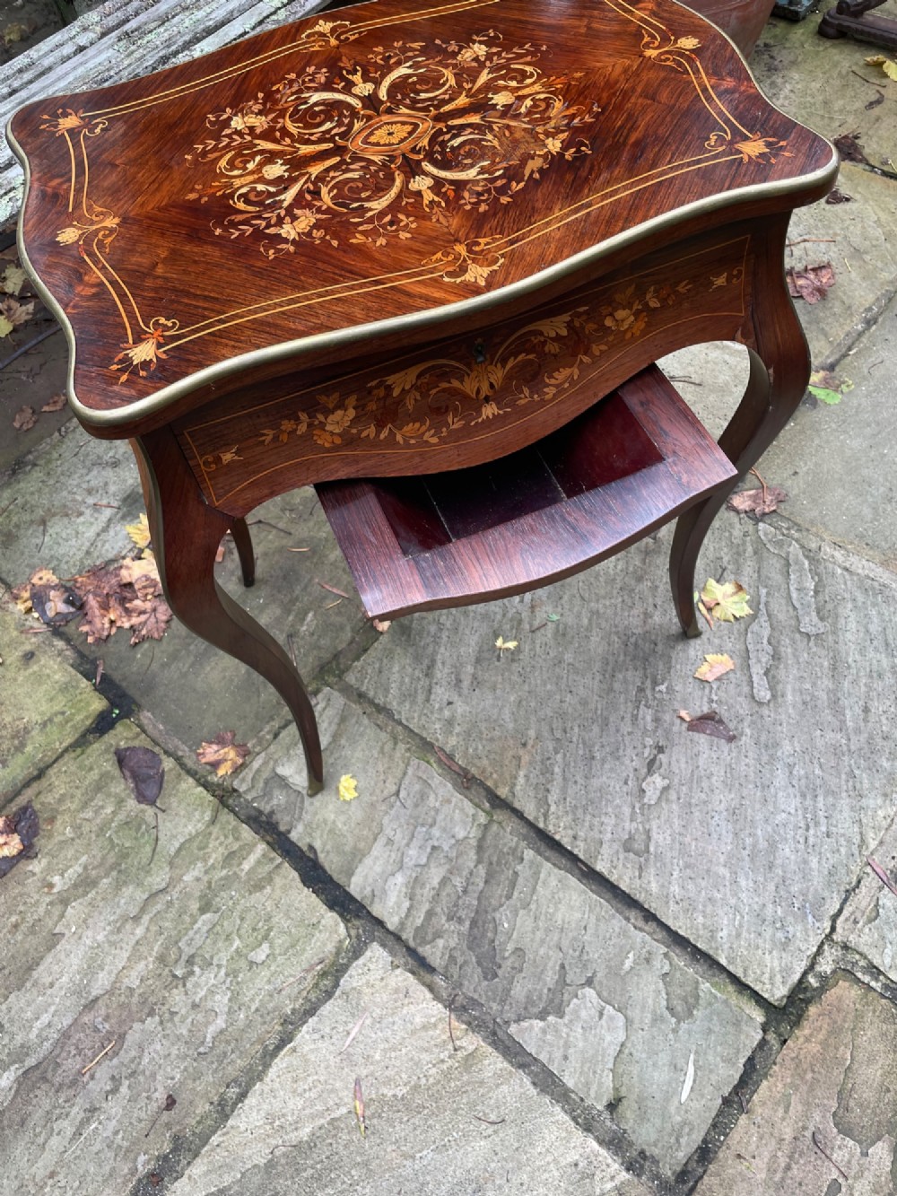 A late 19th-century French marquetry sewing table featuring floral wood inlay on a serpentine top, brass edging, and slender cabriole legs. View IV