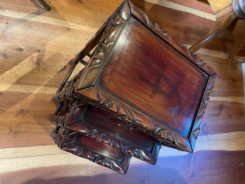 Overhead view of a nest of three dark carved hardwood occasional tables featuring relief-carved borders and recessed tops.