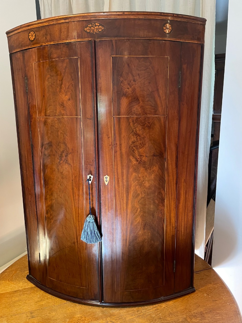 A Georgian mahogany bowfront corner cupboard featuring twin doors and inlaid marquetry motifs.