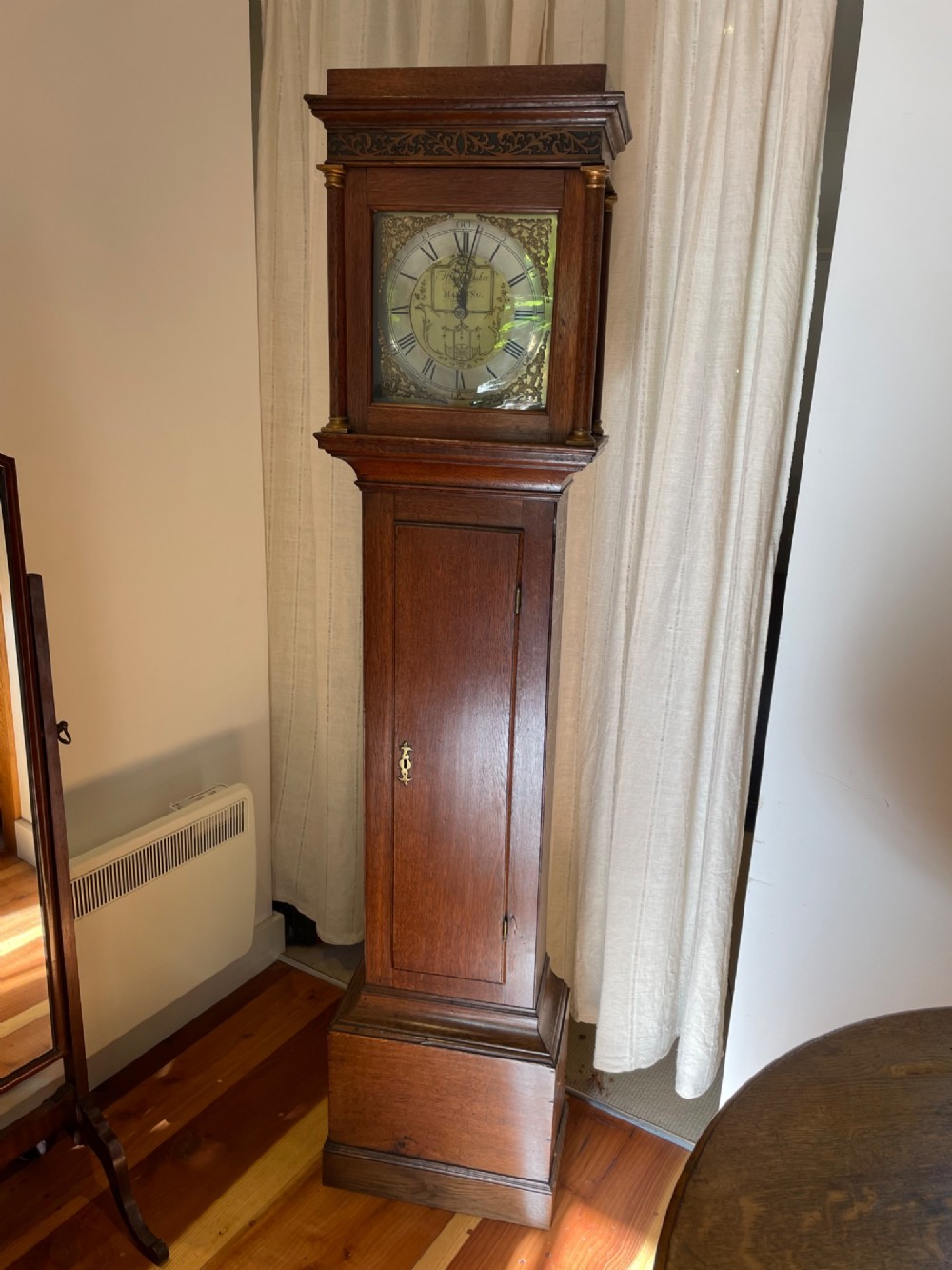 An antique oak longcase grandfather clock featuring a square brass dial with decorative spandrels and a tall timber case.