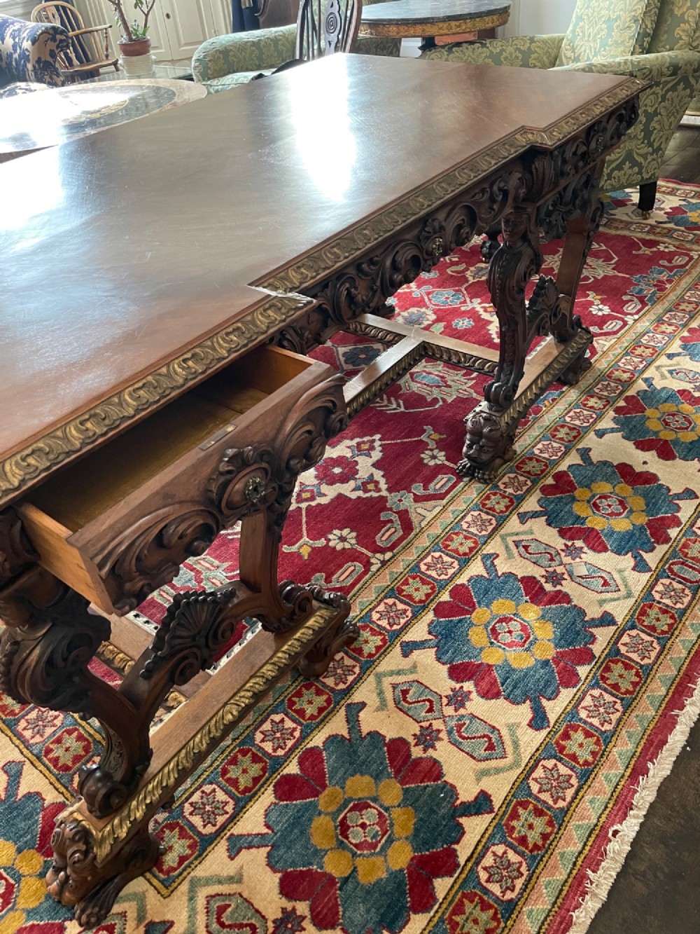 A hand-carved dark walnut Italian desk featuring a rectangular top, carved frieze apron, and ornate trestle legs with figural supports and paw feet. View II