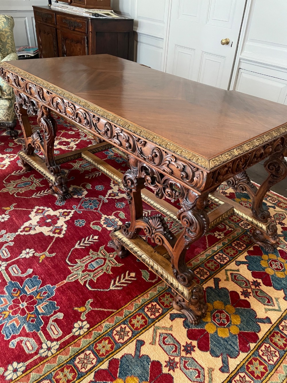 A hand-carved dark walnut Italian desk featuring a rectangular top, carved frieze apron, and ornate trestle legs with figural supports and paw feet. View III