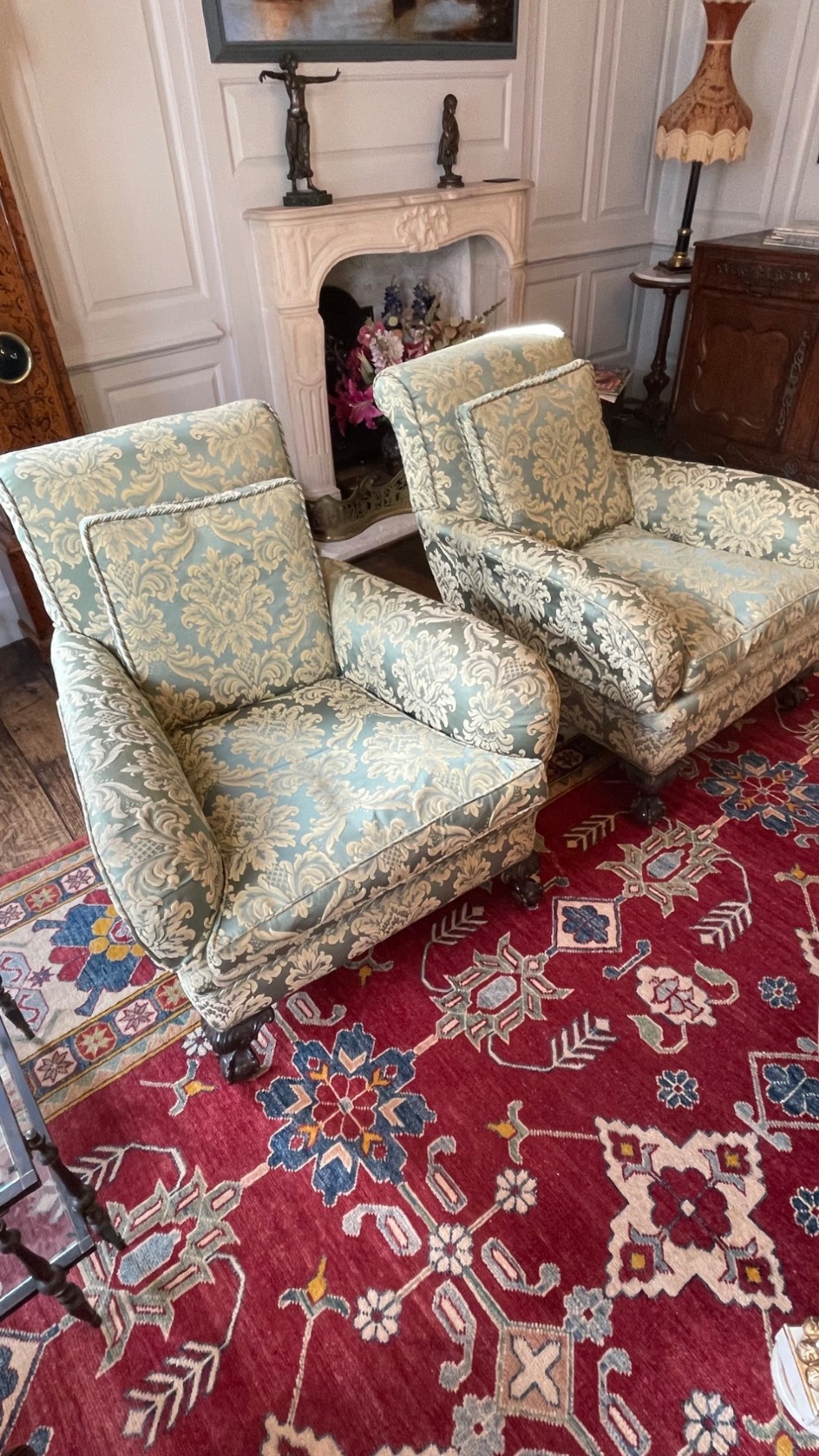A matching pair of fully upholstered armchairs covered in pale blue and cream floral damask fabric with dark turned wooden legs.