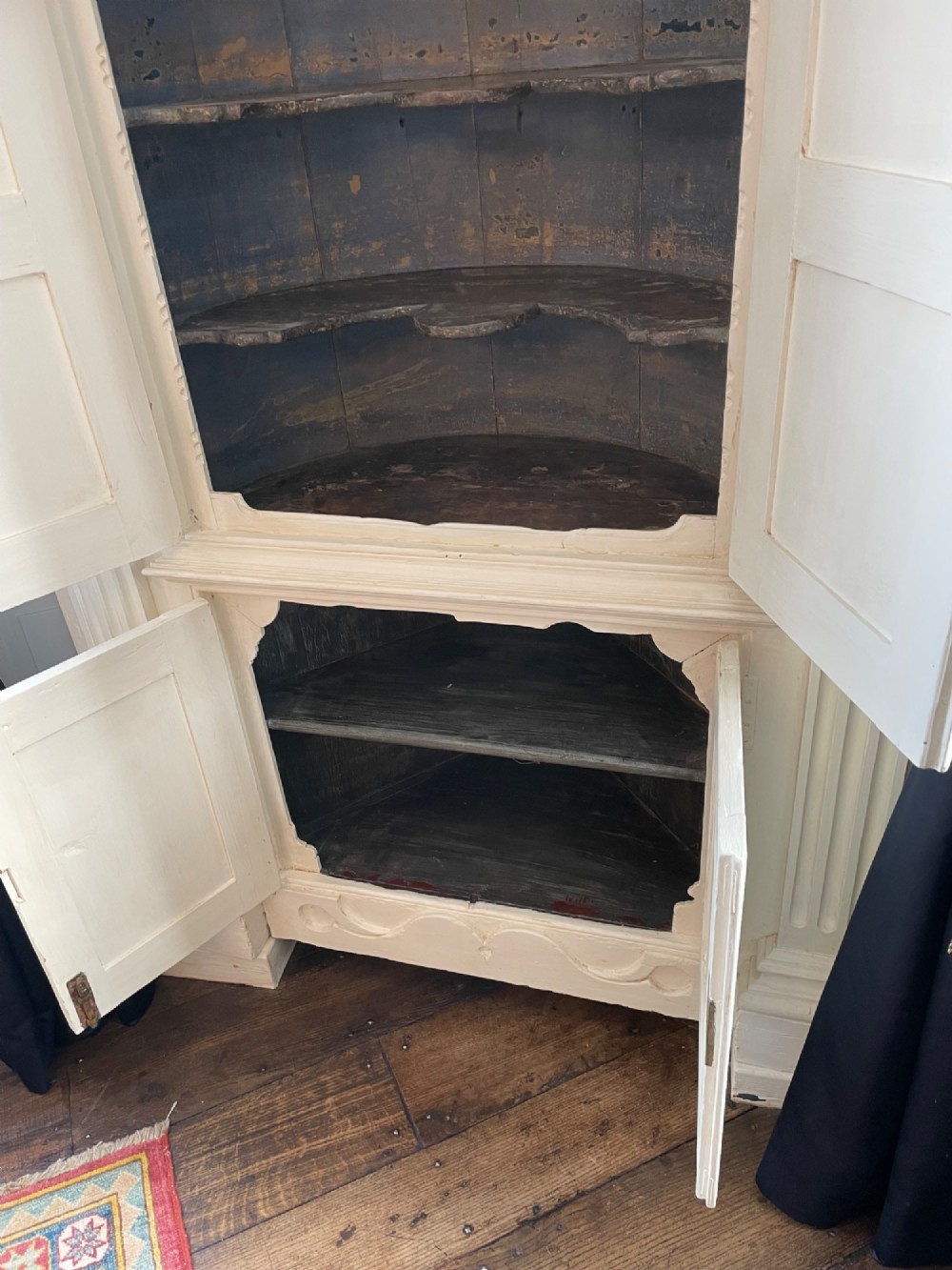 A tall cream-painted pine corner cupboard with open panel doors revealing an arched dark wood shelf interior and lower cabinet. View IV